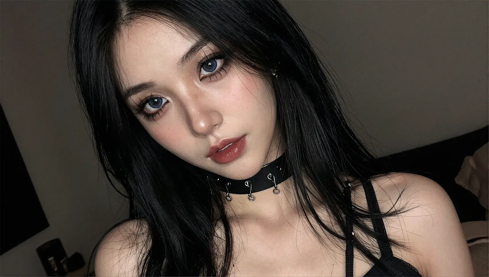 Revealed adult frame: a fictional AI companion in a studded choker, lit by a single bedside lamp